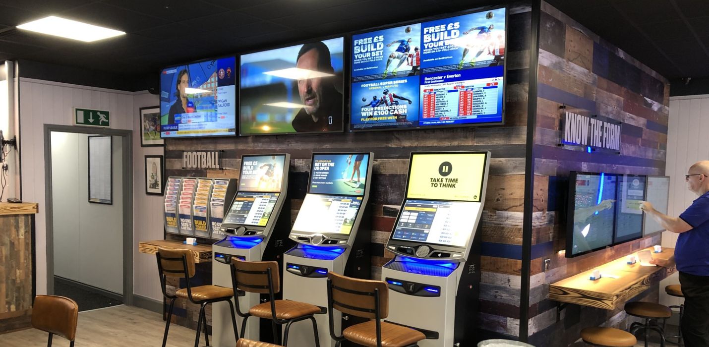 BetStation terminals installed in a Ladbrokes shop — customers using self-service kiosks